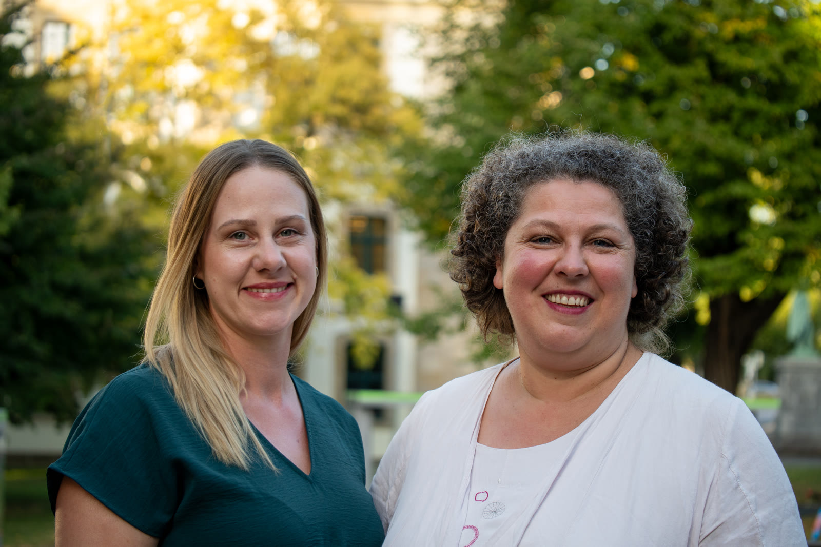 Nicoleta Ion und Annika Höper lächeln gemeinsam in die Kamera, im Hintergrund Bäume im Abendlicht